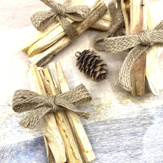 Palo Santo 5 Piece Smudge Sticks bundled in burlap ribbon on a table next to a pine cone